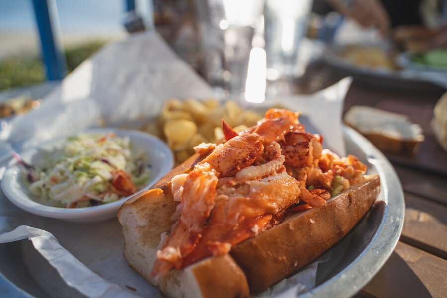 Overflowing New England lobster roll served with coleslaw and kettle chips at a waterfront table, Boston