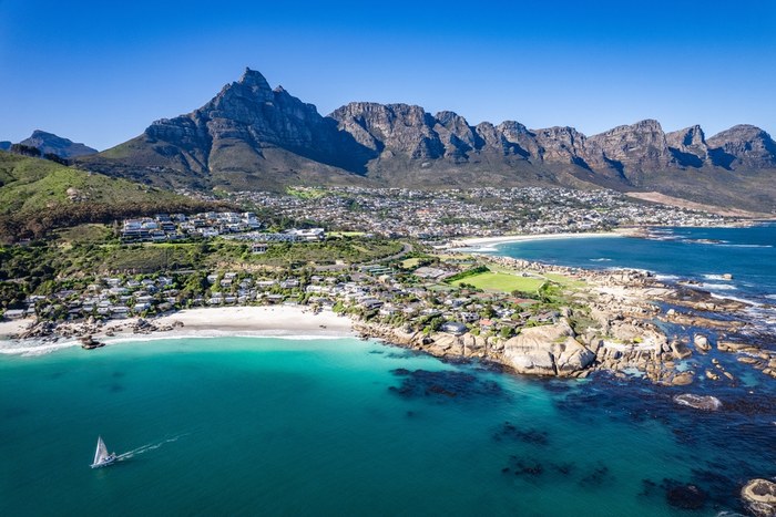 Aerial view of Clifton beach and the Twelve Apostles mountain range in Cape Town, with a yacht sailing in turquoise water