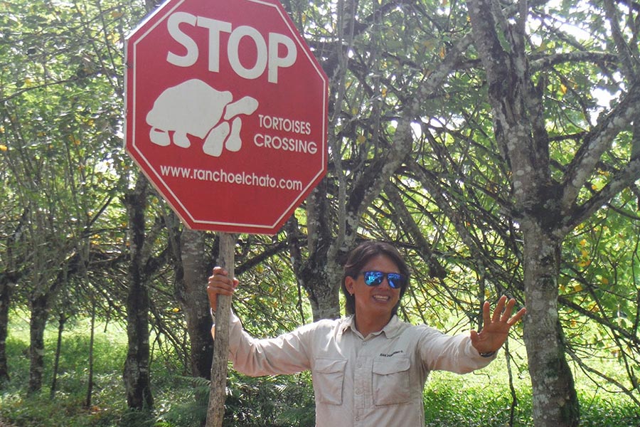Tour guide in sunglasses posing playfully next to a tortoise crossing road sign in Galapagos