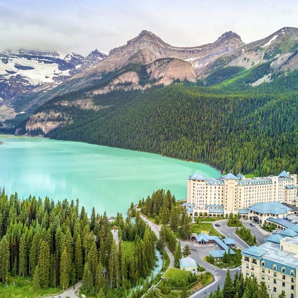 Aerial view of turquoise Lake Louise surrounded by pine forest, with the Fairmont Chateau Lake Louise on the shoreline and the glacier-capped peaks of Banff National Park behind