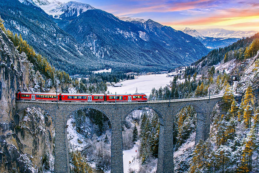 Red panoramic train crossing a stone viaduct in a snow-covered Alpine valley