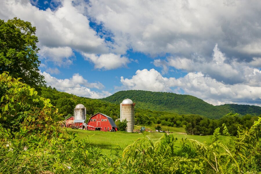 Red barn and silos set against green rolling hills and summer clouds in the Vermont countryside